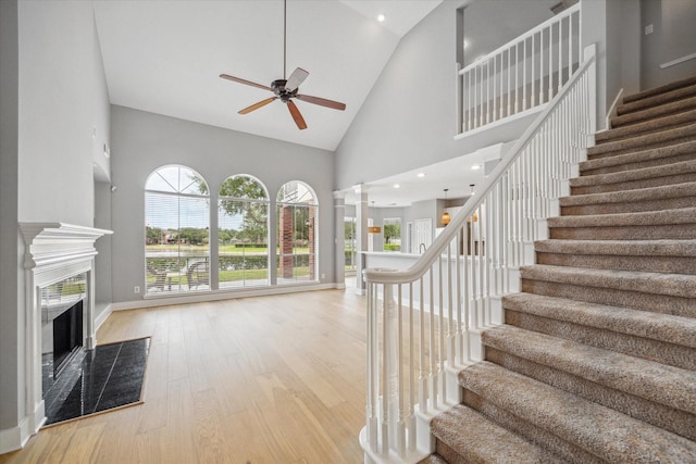 interior space featuring decorative columns, ceiling fan, wood finished floors, high vaulted ceiling, and a high end fireplace