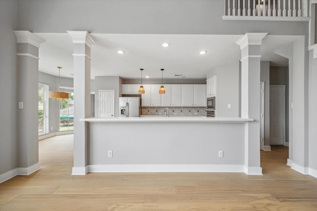 kitchen featuring decorative light fixtures, stainless steel appliances, light countertops, ornate columns, and white cabinetry