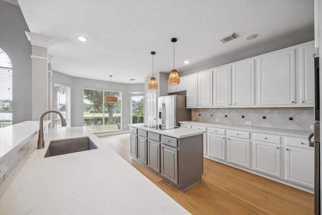 kitchen with stainless steel fridge, hanging light fixtures, light countertops, white cabinetry, and a sink