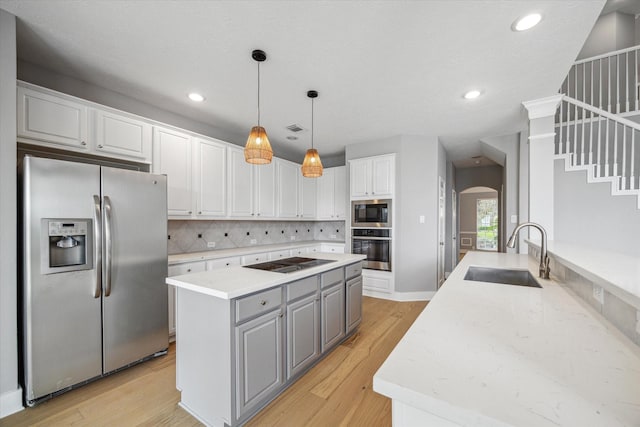 kitchen featuring arched walkways, white cabinets, decorative light fixtures, black appliances, and a sink