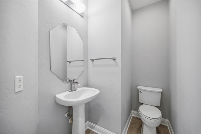 half bath with toilet, tile patterned flooring, baseboards, and a sink