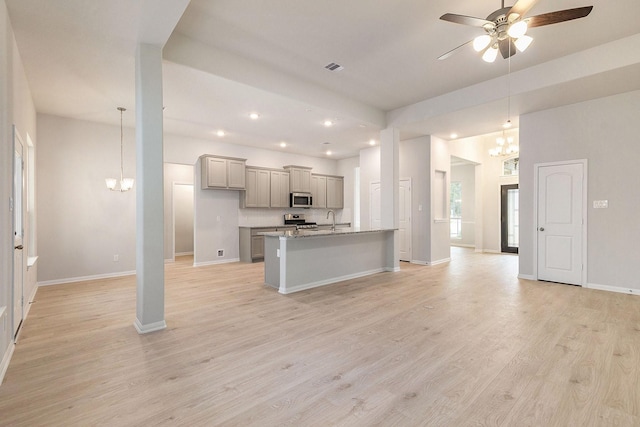 kitchen featuring gray cabinetry, stainless steel appliances, light stone countertops, an island with sink, and pendant lighting