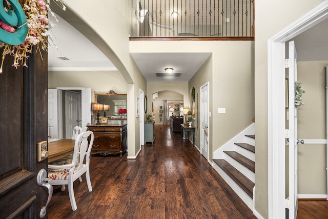 foyer with arched walkways, visible vents, a towering ceiling, dark wood-type flooring, and baseboards