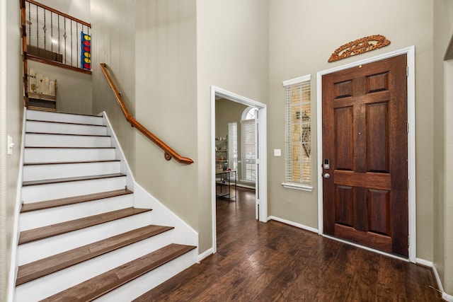 entrance foyer featuring a towering ceiling, dark wood finished floors, stairway, and baseboards