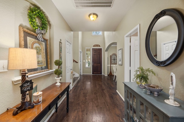 foyer entrance featuring arched walkways, dark wood-style flooring, visible vents, and baseboards