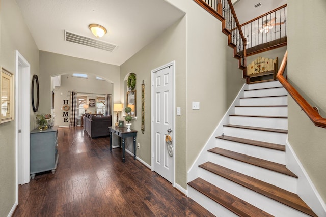 entrance foyer featuring stairway, baseboards, arched walkways, and dark wood-style flooring