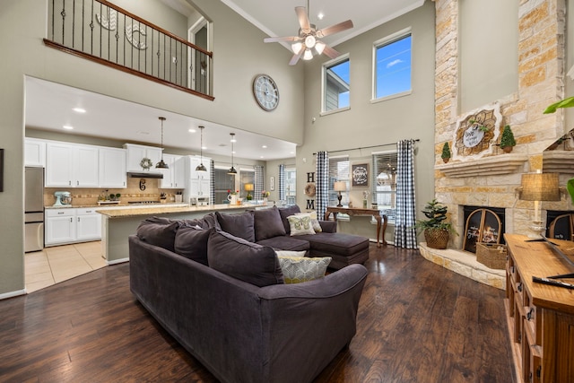 living room with ceiling fan, crown molding, a stone fireplace, and wood finished floors