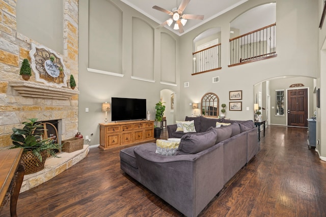 living area with dark wood-style floors, arched walkways, a fireplace, visible vents, and a ceiling fan