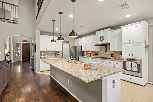 kitchen featuring visible vents, white cabinets, appliances with stainless steel finishes, a center island with sink, and pendant lighting