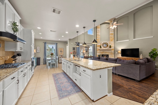 kitchen with a kitchen island with sink, white cabinetry, stainless steel gas cooktop, and hanging light fixtures