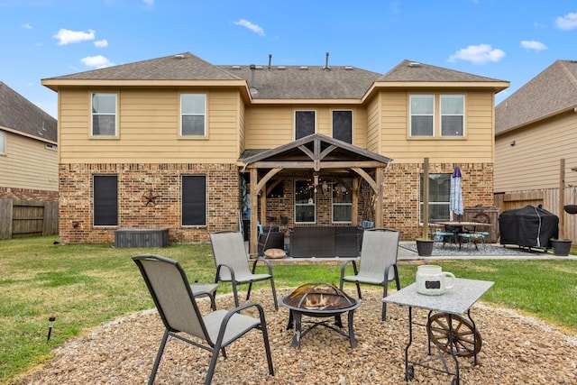 rear view of house with a yard, an outdoor fire pit, fence, and brick siding