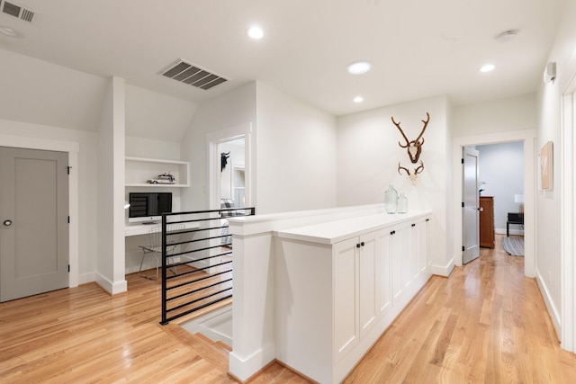 hallway with light wood-style flooring, an upstairs landing, and visible vents