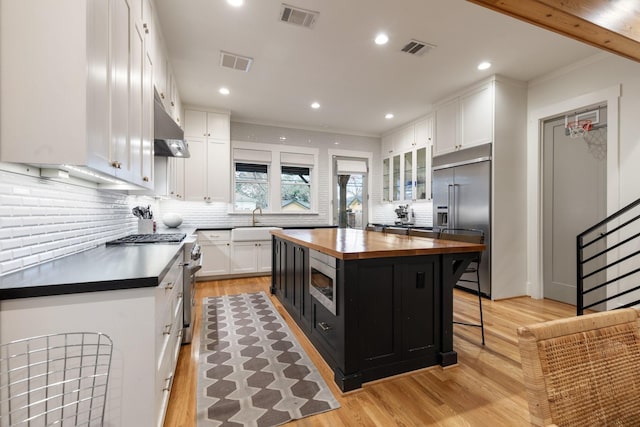 kitchen with visible vents, white cabinets, high quality appliances, glass insert cabinets, and a center island