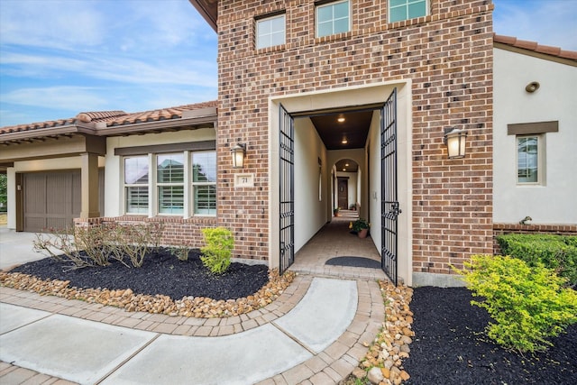 entrance to property with a garage, stucco siding, a tile roof, and brick siding