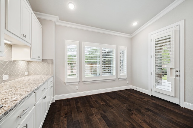 kitchen with dark wood-style floors, light stone counters, ornamental molding, white cabinetry, and backsplash