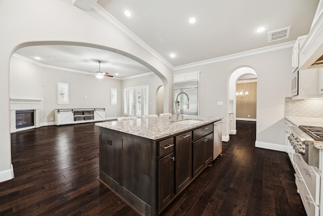 kitchen with appliances with stainless steel finishes, open floor plan, a kitchen island with sink, dark brown cabinetry, and a sink