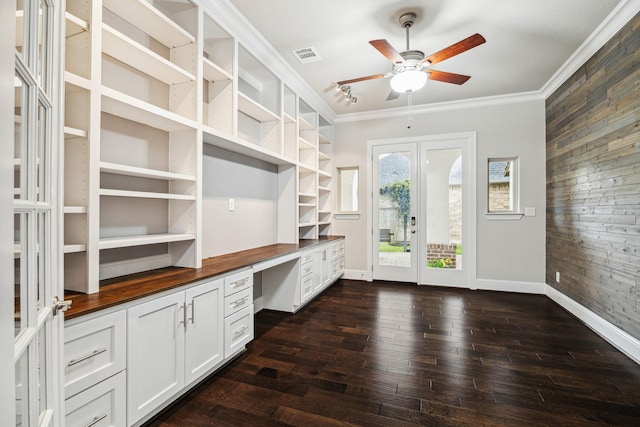 unfurnished office with wood walls, visible vents, ornamental molding, built in desk, and dark wood finished floors