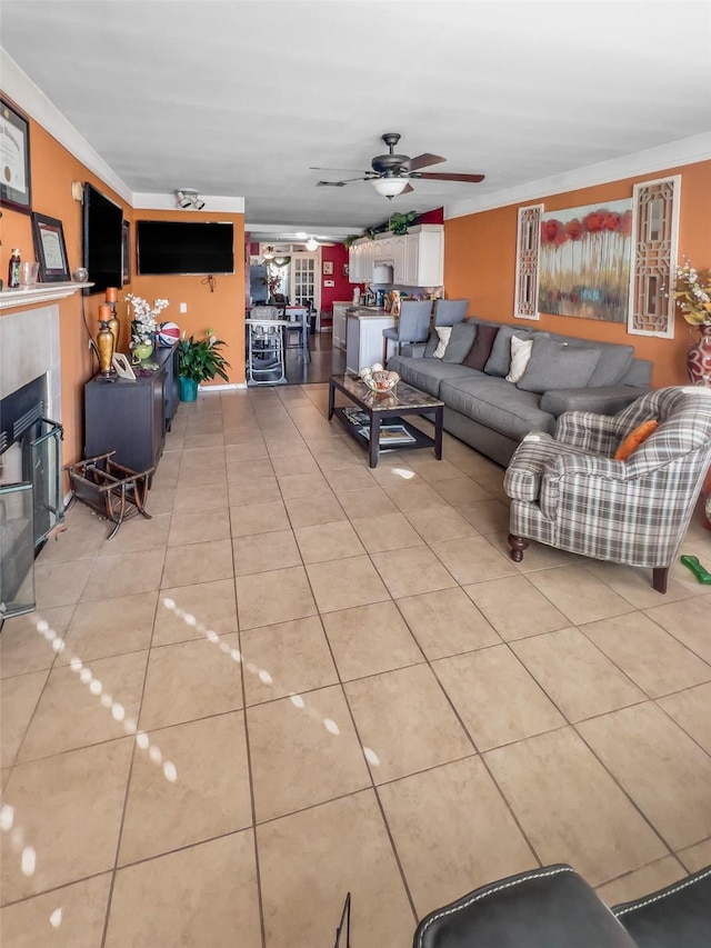 living area featuring light tile patterned floors, ornamental molding, a ceiling fan, and a glass covered fireplace