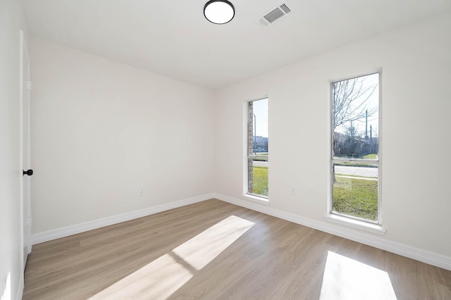 empty room featuring light wood-style flooring, visible vents, and baseboards