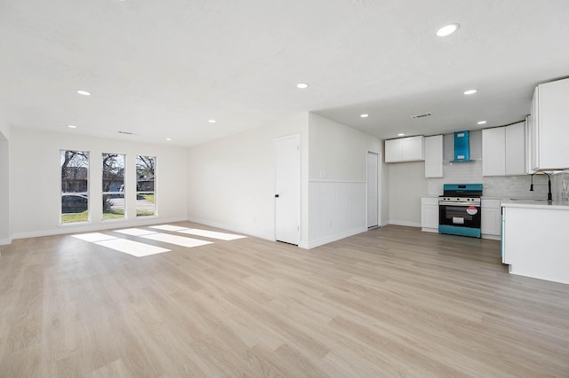 unfurnished living room with baseboards, visible vents, light wood-type flooring, a sink, and recessed lighting