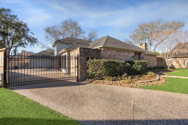 exterior space featuring concrete driveway, a chimney, a gate, fence, and brick siding