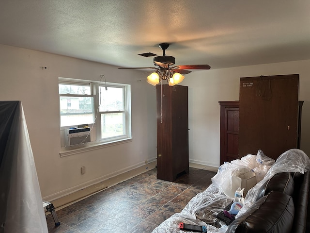 bedroom featuring cooling unit, baseboards, ceiling fan, stone finish floor, and a textured ceiling