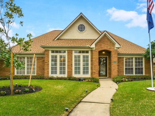 view of front of property with brick siding, roof with shingles, and a front yard