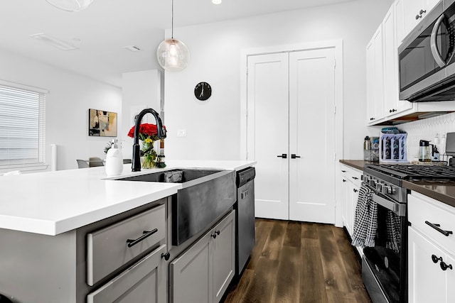 kitchen with stainless steel appliances, dark wood-type flooring, a sink, white cabinets, and hanging light fixtures