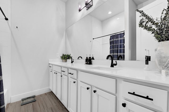 full bathroom featuring double vanity, baseboards, a sink, and wood finished floors