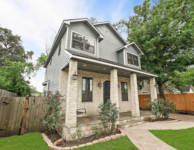 view of front of home with covered porch, stone siding, and fence