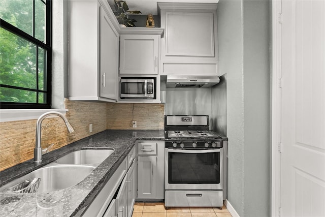 kitchen with tasteful backsplash, appliances with stainless steel finishes, a sink, dark stone countertops, and ventilation hood