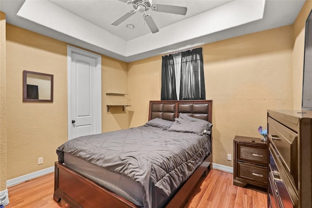 bedroom with a textured wall, a tray ceiling, light wood-type flooring, and baseboards