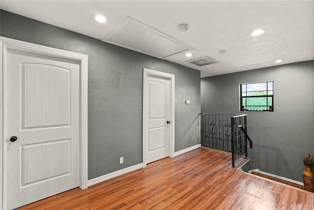 empty room with attic access, baseboards, visible vents, a textured wall, and wood finished floors