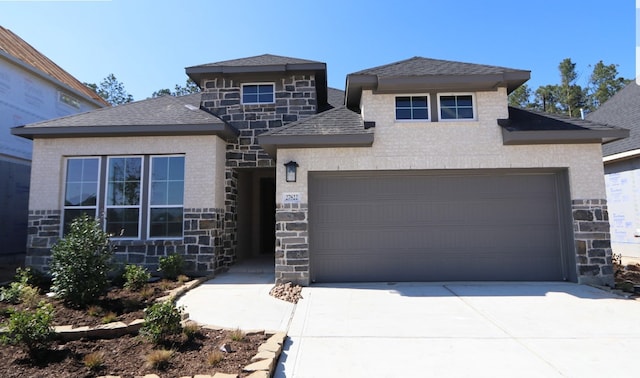 view of front of home featuring a garage, stone siding, a shingled roof, and concrete driveway