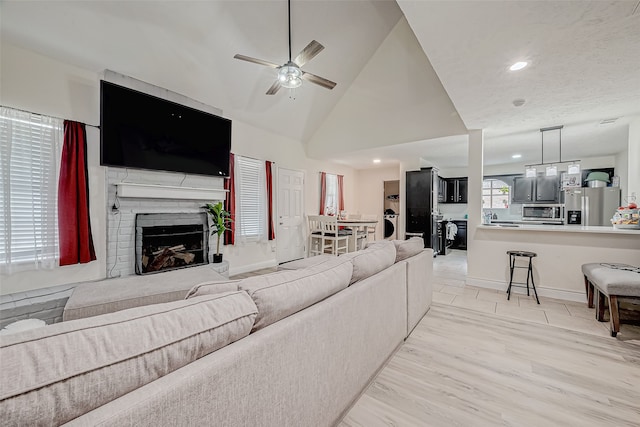 living area featuring baseboards, ceiling fan, light wood-type flooring, a brick fireplace, and recessed lighting