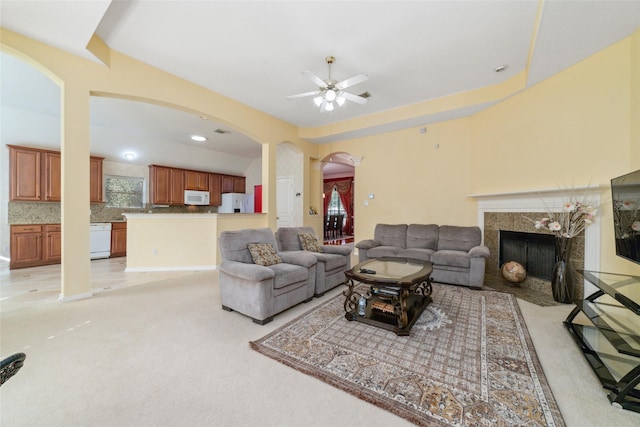 living area with ceiling fan, arched walkways, light colored carpet, and a high end fireplace