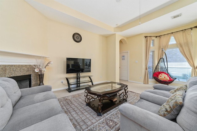 living area featuring arched walkways, light colored carpet, visible vents, baseboards, and a tiled fireplace