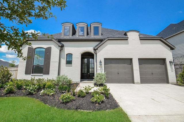 french country inspired facade with driveway, brick siding, and an attached garage