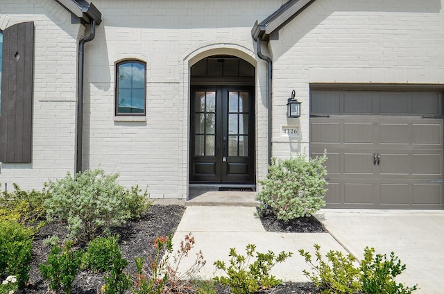 view of exterior entry featuring brick siding, french doors, driveway, and a garage