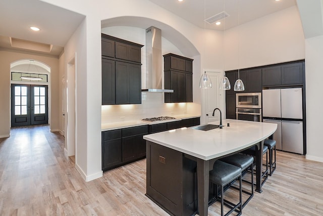 kitchen featuring wall chimney range hood, decorative backsplash, arched walkways, stainless steel appliances, and a sink