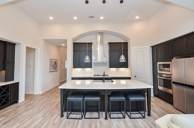 kitchen with stainless steel appliances, wall chimney exhaust hood, backsplash, and a breakfast bar area