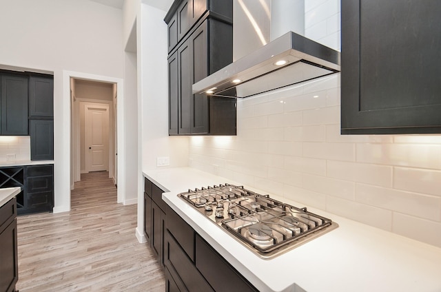 kitchen with stainless steel gas cooktop, light wood finished floors, light countertops, and wall chimney range hood