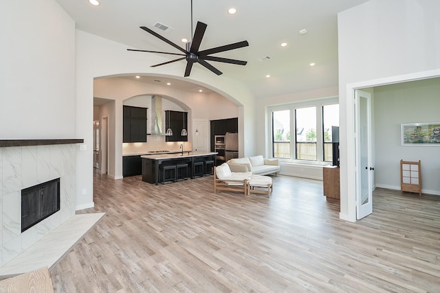 living area with visible vents, high vaulted ceiling, light wood-style flooring, a ceiling fan, and arched walkways