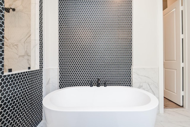 full bath featuring a soaking tub, marble finish floor, and tile walls