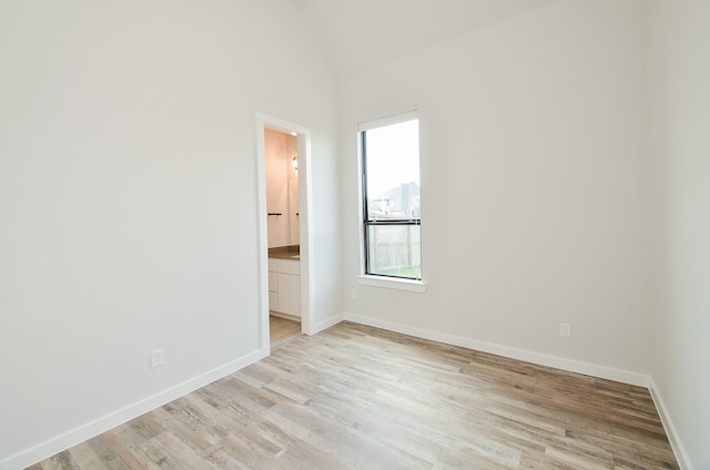 spare room with lofted ceiling, light wood-style floors, and baseboards