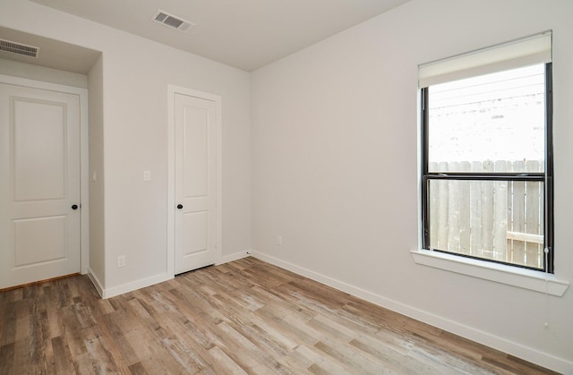 spare room featuring light wood-type flooring, visible vents, and baseboards