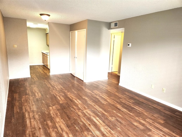 unfurnished room with baseboards, dark wood-style flooring, a textured ceiling, and visible vents