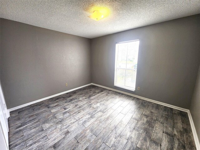 empty room with baseboards, dark wood finished floors, and a textured ceiling
