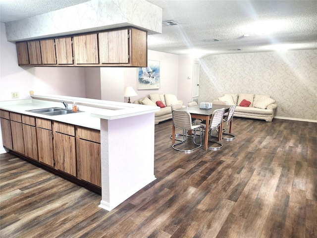 kitchen featuring a peninsula, open floor plan, a textured ceiling, a sink, and dark wood finished floors