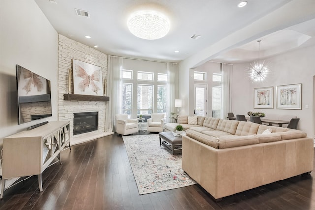 living area featuring a stone fireplace, dark wood finished floors, visible vents, and a notable chandelier